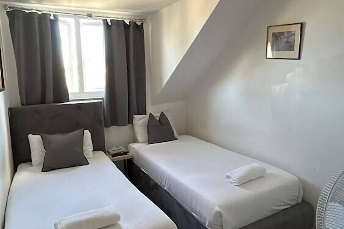 Une chambre avec deux lits, un ventilateur de plafond, une petite table et une fenêtre avec des rideaux.