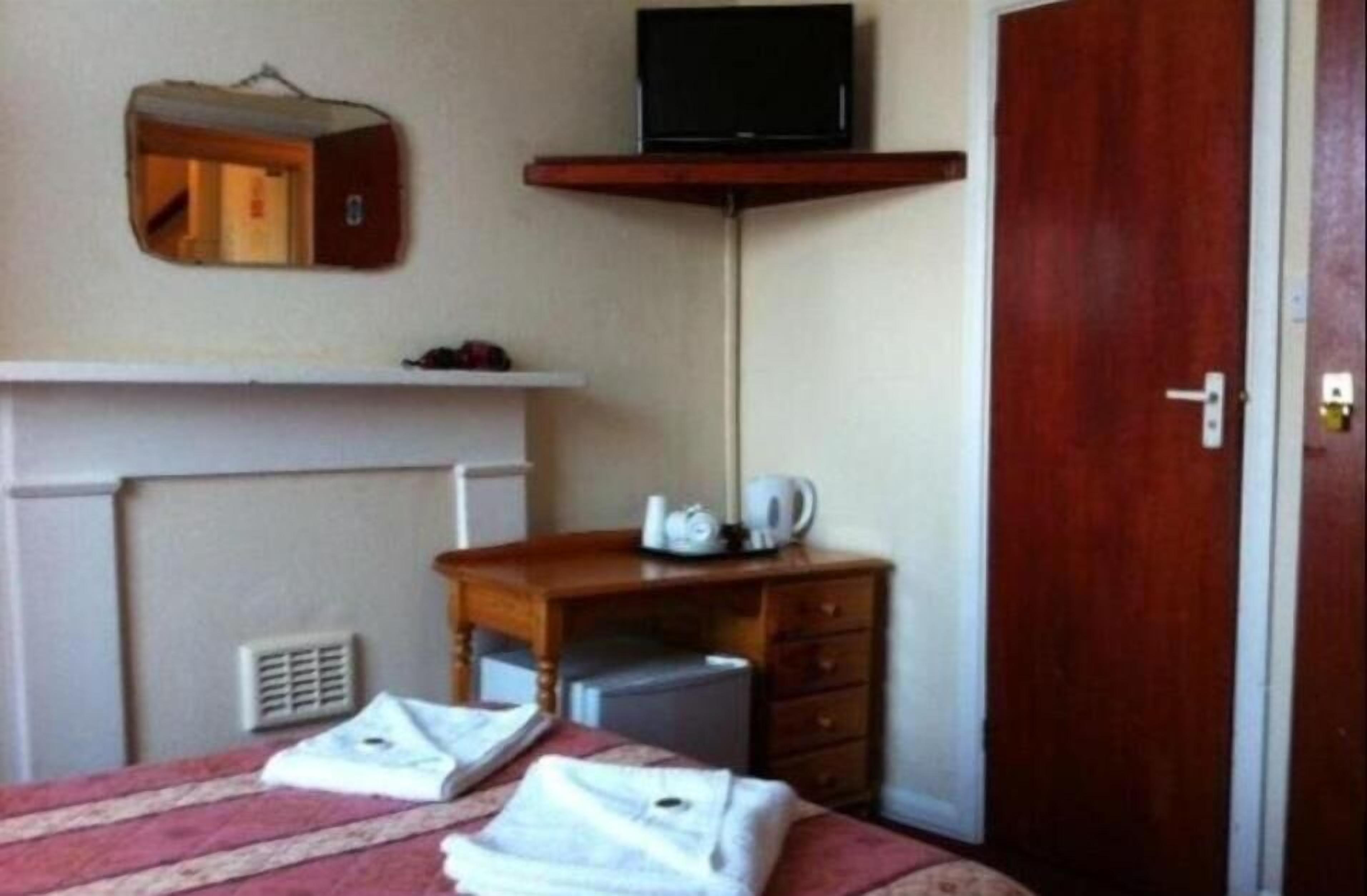 Habitación de hotel con cama, escritorio, televisor, armario y puerta.