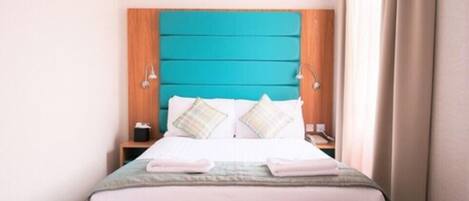 A neatly made bed with a teal headboard, two bedside tables, and a window with curtains.