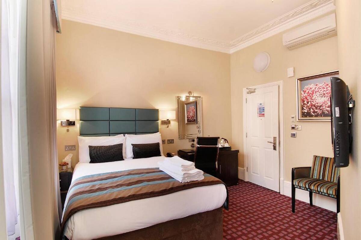 A hotel room with a large bed, a television, a desk, and a chair.