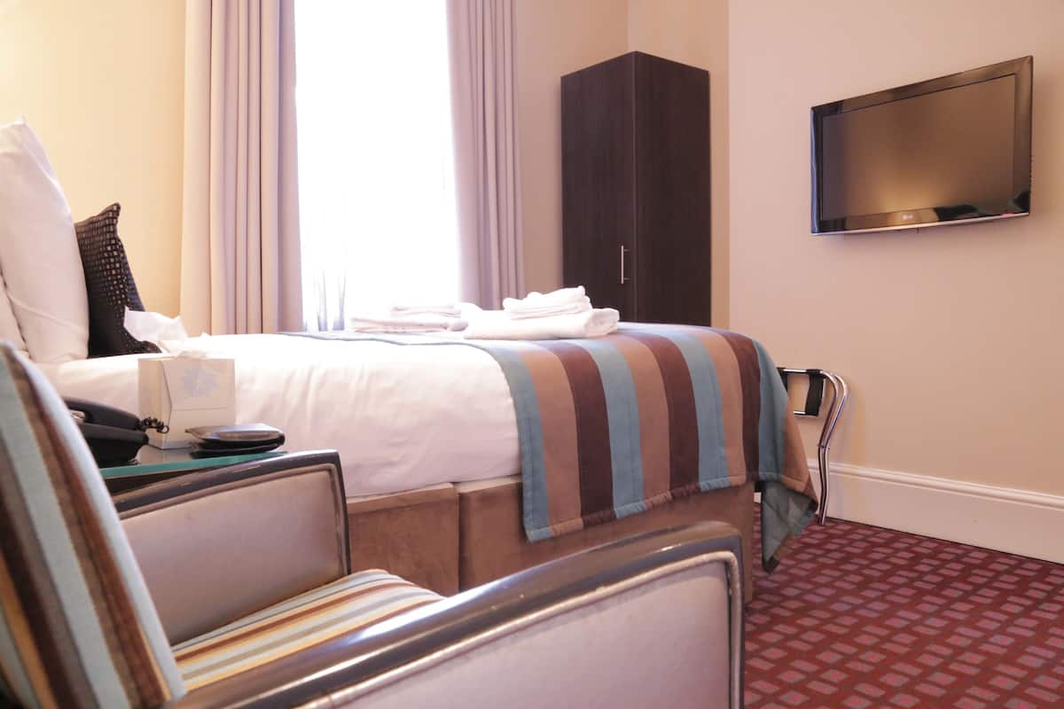 A hotel room with a bed, a TV mounted on the wall, a bedside table with a phone, and a window with curtains.