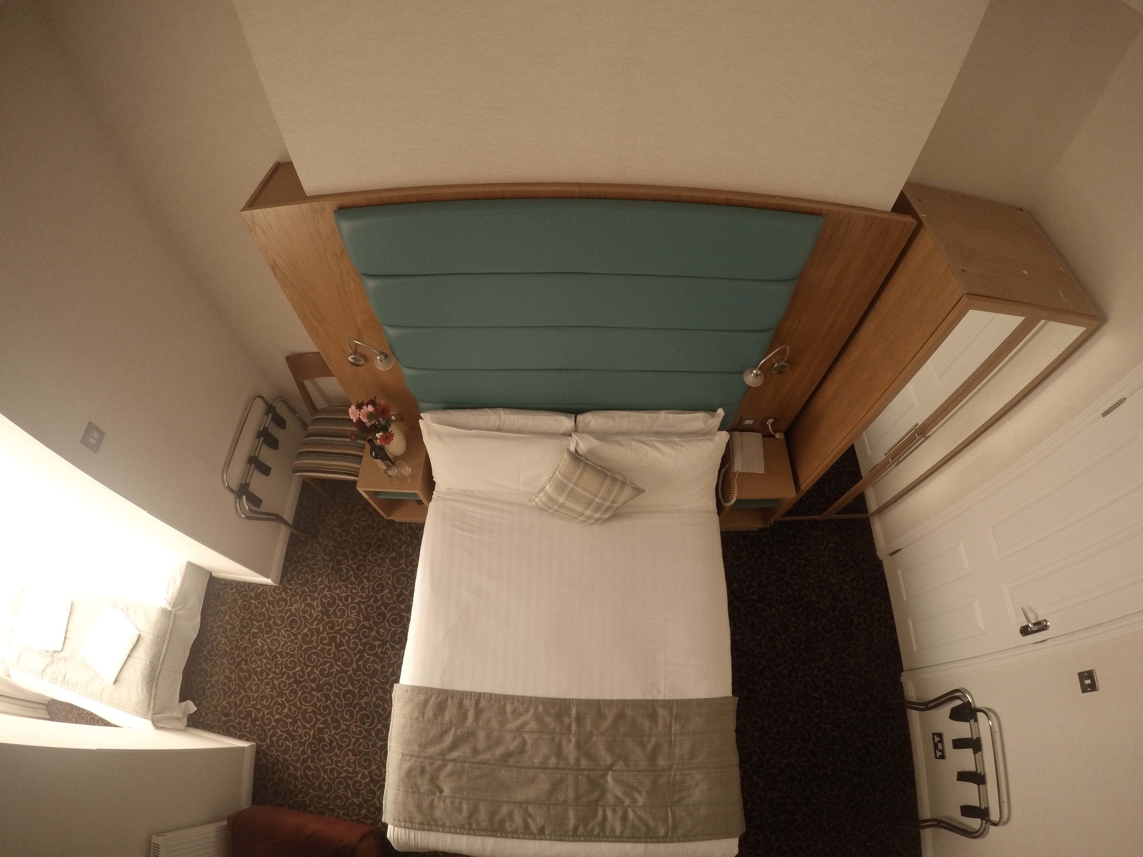 Quarto de hotel pequeno com uma cama, uma mesinha de cabeceira, um espelho e uma porta.
