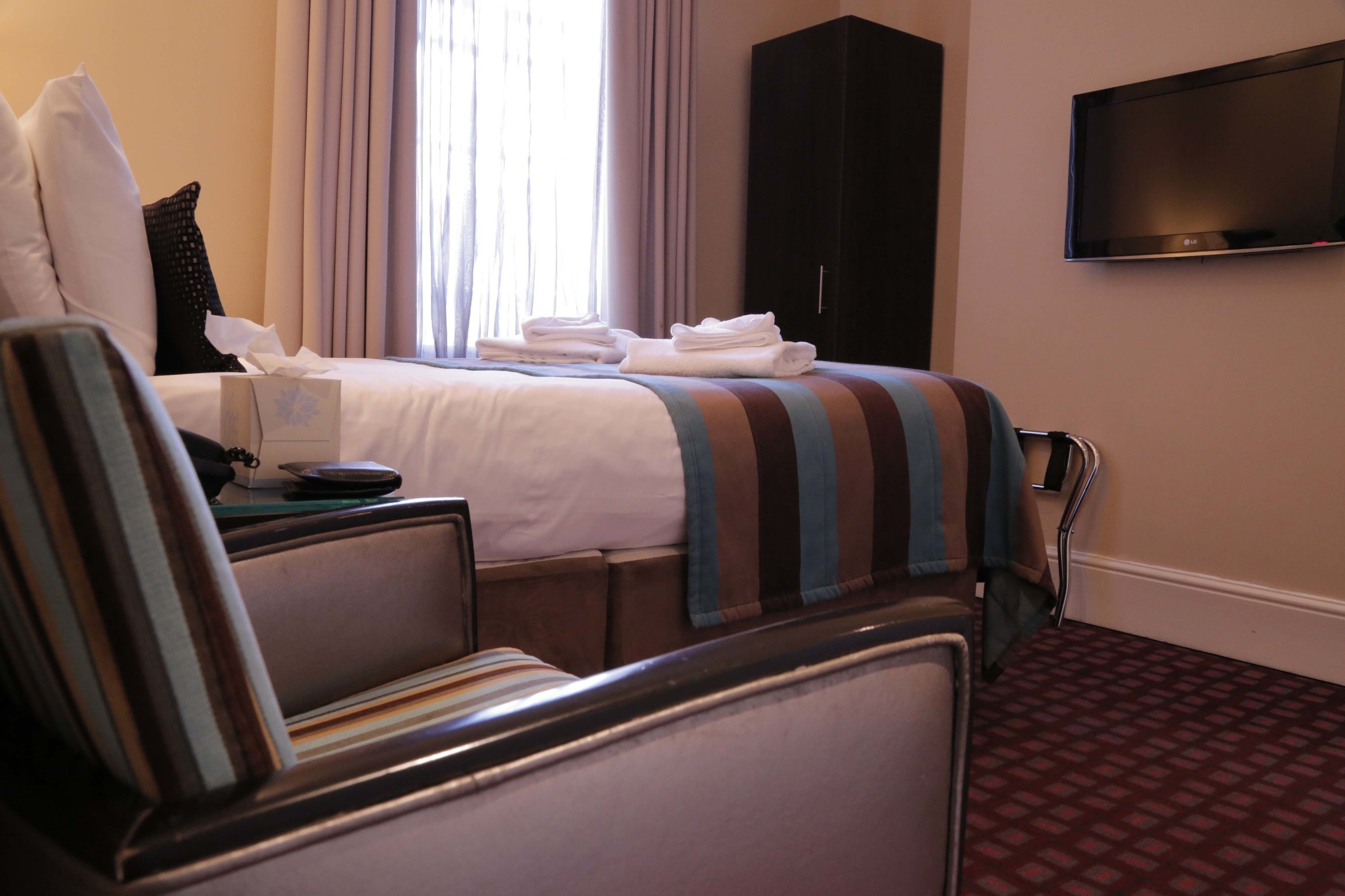 A hotel room with a bed, a TV mounted on the wall, a desk with a lamp, and a chair.