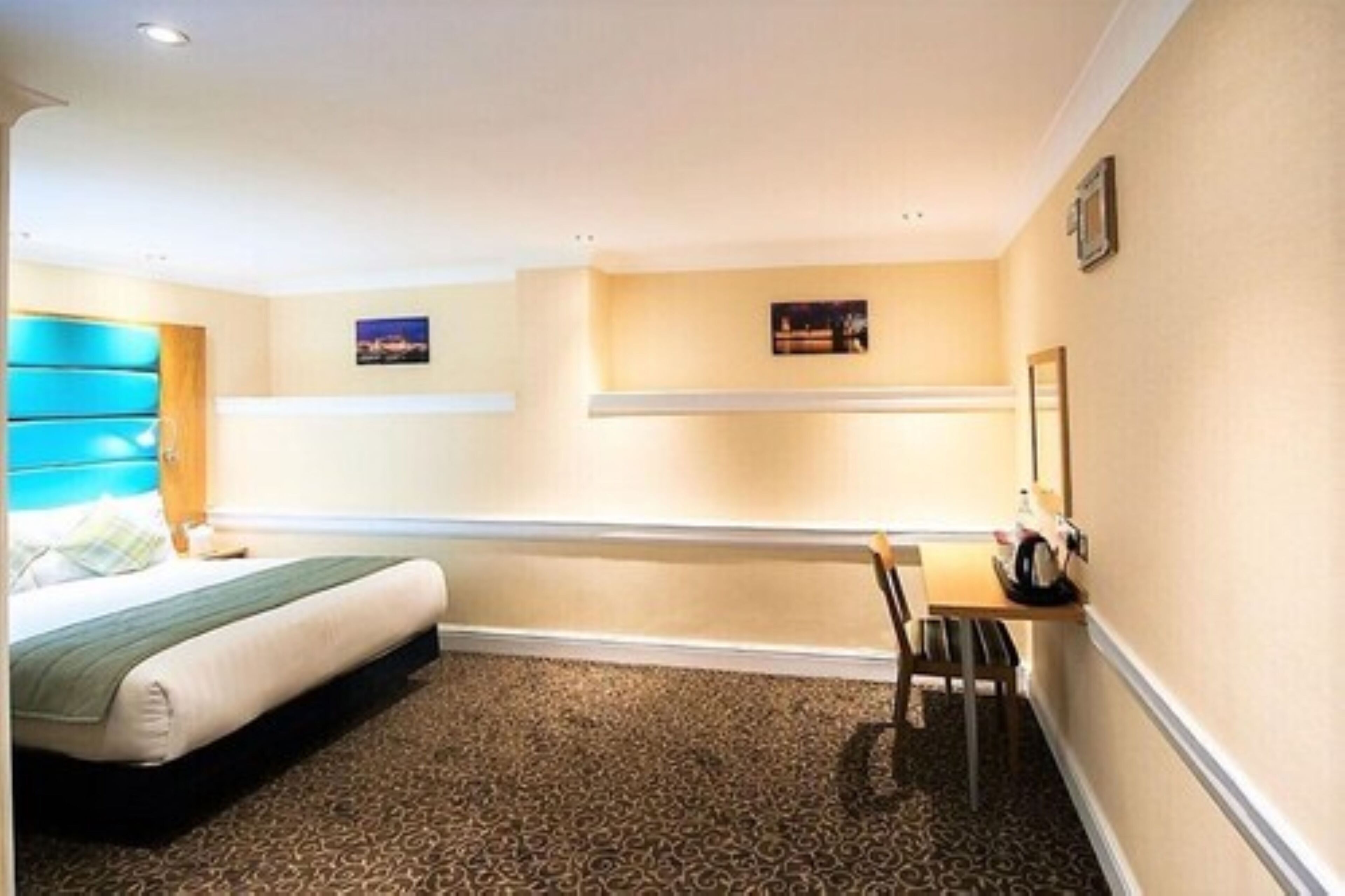 A hotel room with a bed, a desk, a chair, and two framed pictures on the wall.