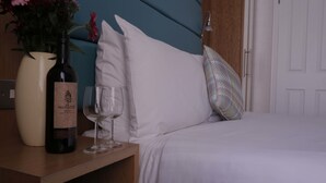 A hotel room with a bed, a bedside table with a bottle of wine, a glass, and a vase of flowers. - Astors Belgravia (London)