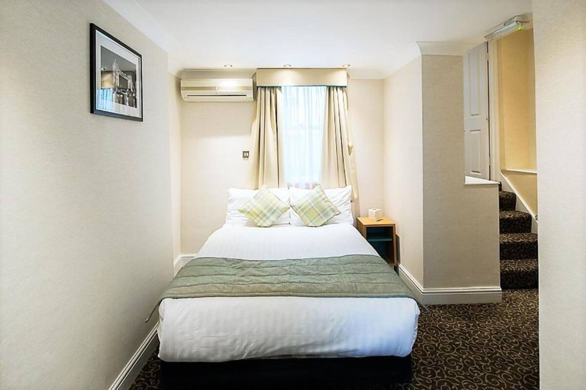 A hotel room with a bed, a nightstand, a framed picture on the wall, and a window with curtains.