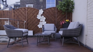 A patio with wicker furniture, a wooden fence, and a potted plant. - Astors Belgravia (London)