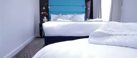 Een hotelkamer met twee bedden, een blauw hoofdbord en een klein nachtkastje met een bloevas.