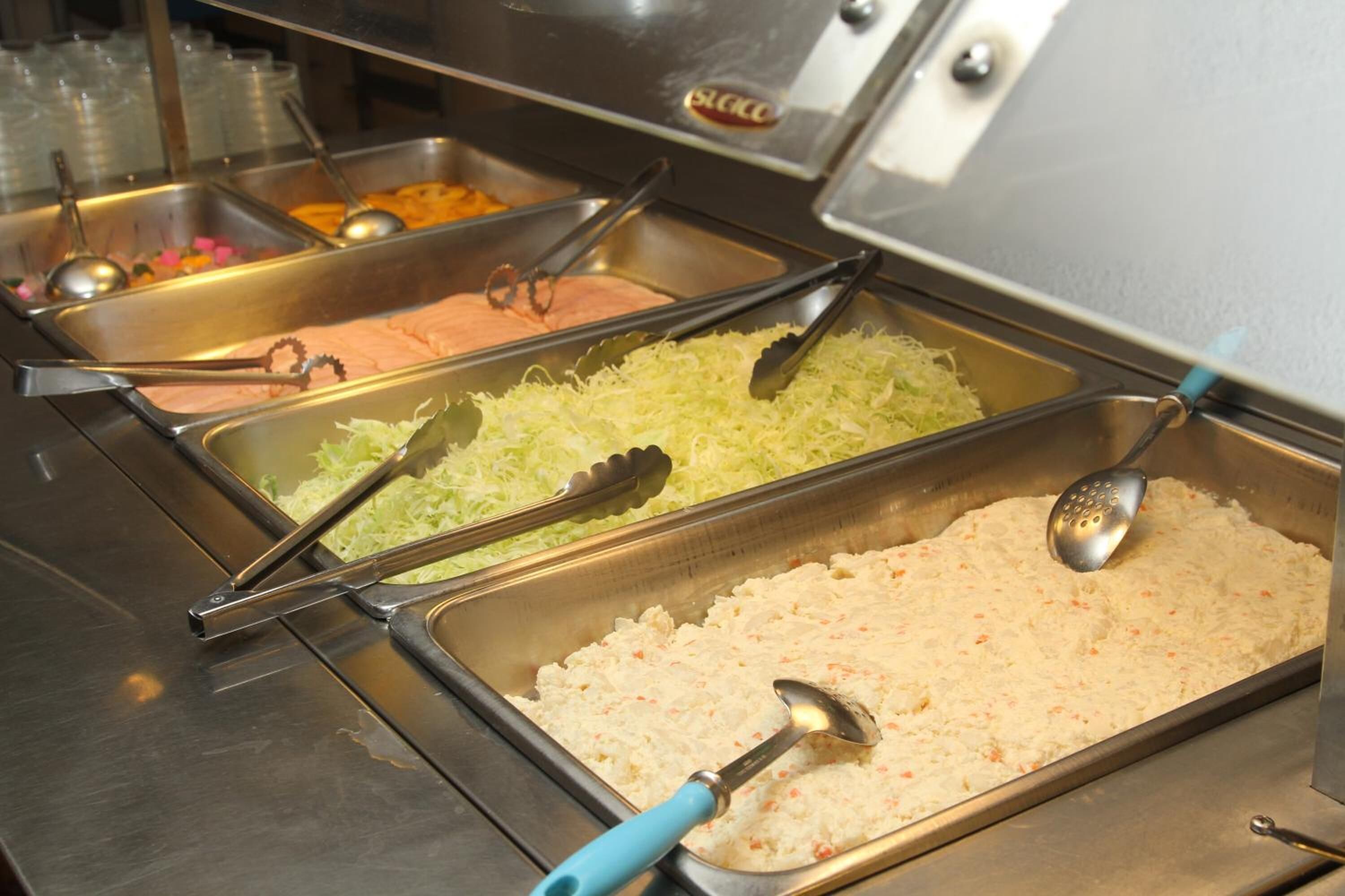 A buffet with various food options, including shredded vegetables and a creamy dish, served in metal trays with serving utensils.