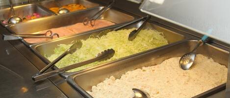 A buffet with various food options, including shredded vegetables and a creamy dish, served in metal trays with serving utensils.