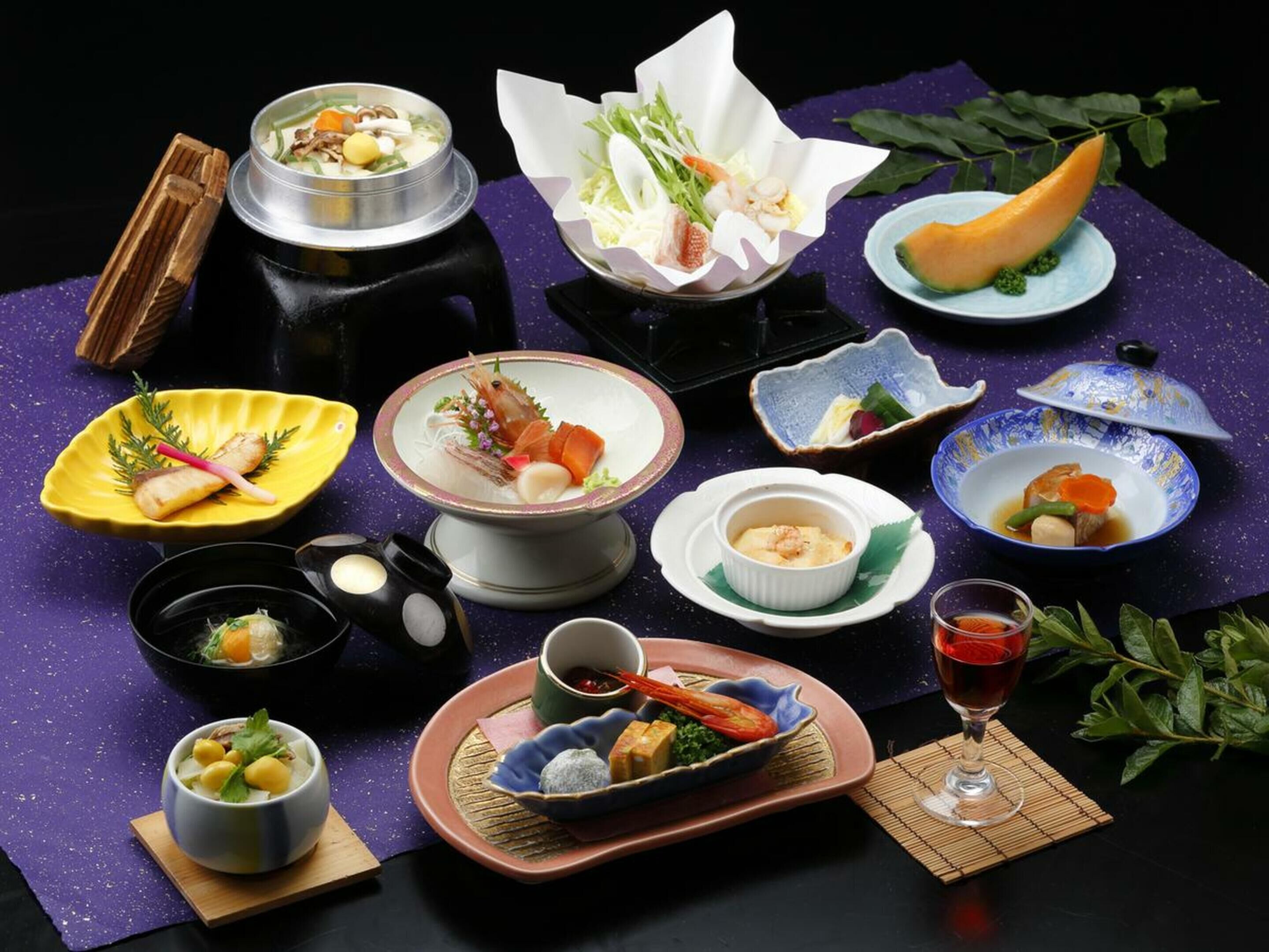 A variety of dishes and a glass of red wine on a table with a dark background.