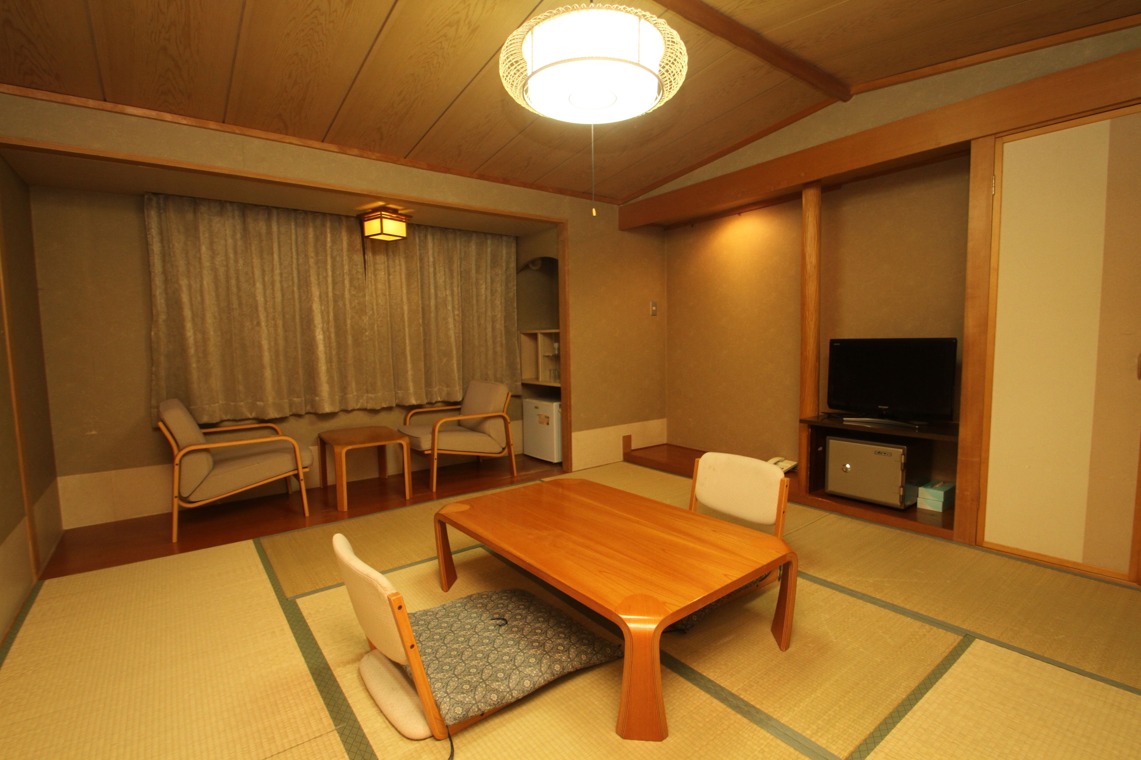 A traditional Japanese-style room with tatami flooring, a low wooden table, a television, and a sliding door.