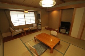 Una habitación tradicional japonesa con suelo de tatami, una mesa de madera para comer, un televisor y una puerta corredera.