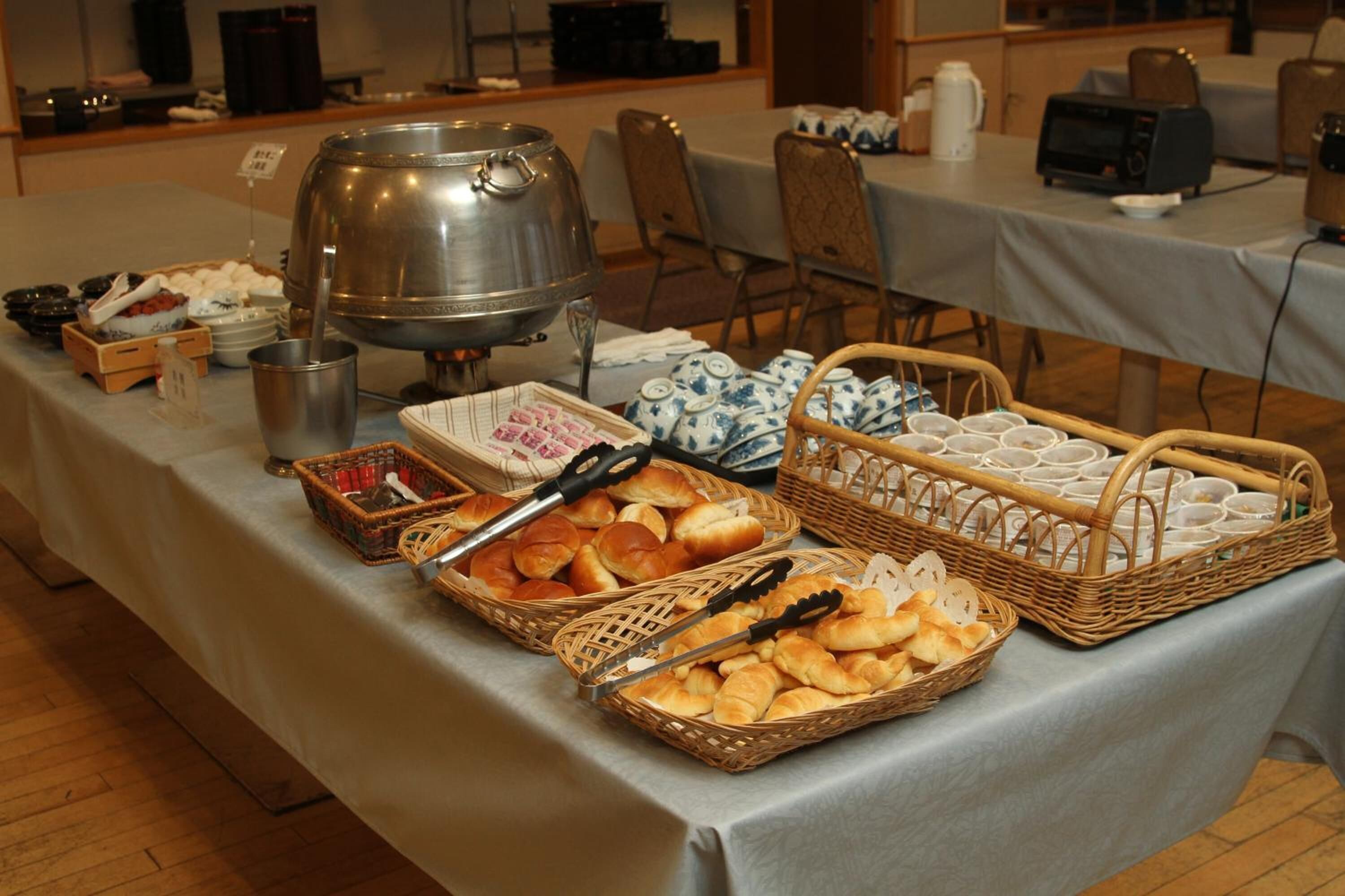 Une table de buffet proposant divers aliments, notamment du pain, des pâtisseries et un grand récipient en métal, probablement destiné aux boissons chaudes.