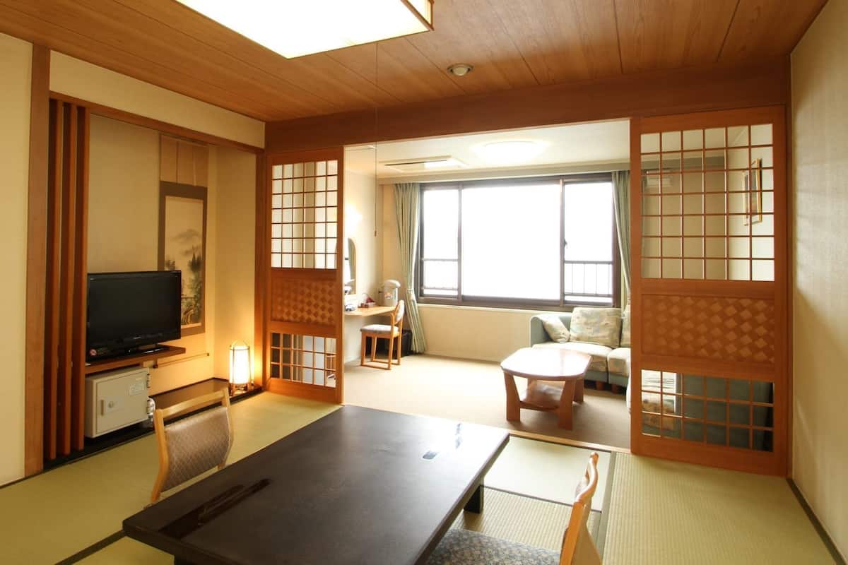 Ett traditionellt japanskt rum med tatamimattor på golvet, en tv, ett skrivbord med en stol och en soffa.