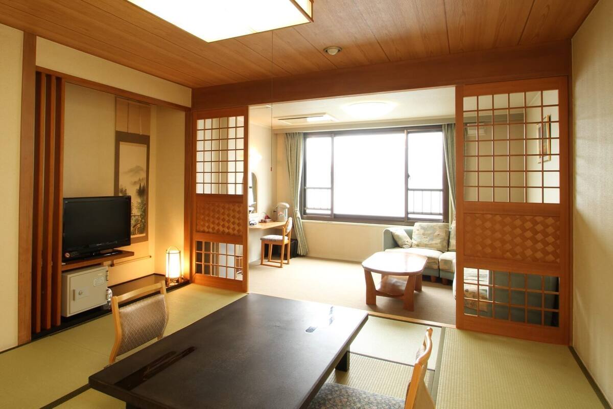 Une pièce de style japonais traditionnel, avec un sol recouvert de tatamis, une télévision, un bureau avec une chaise et un canapé.