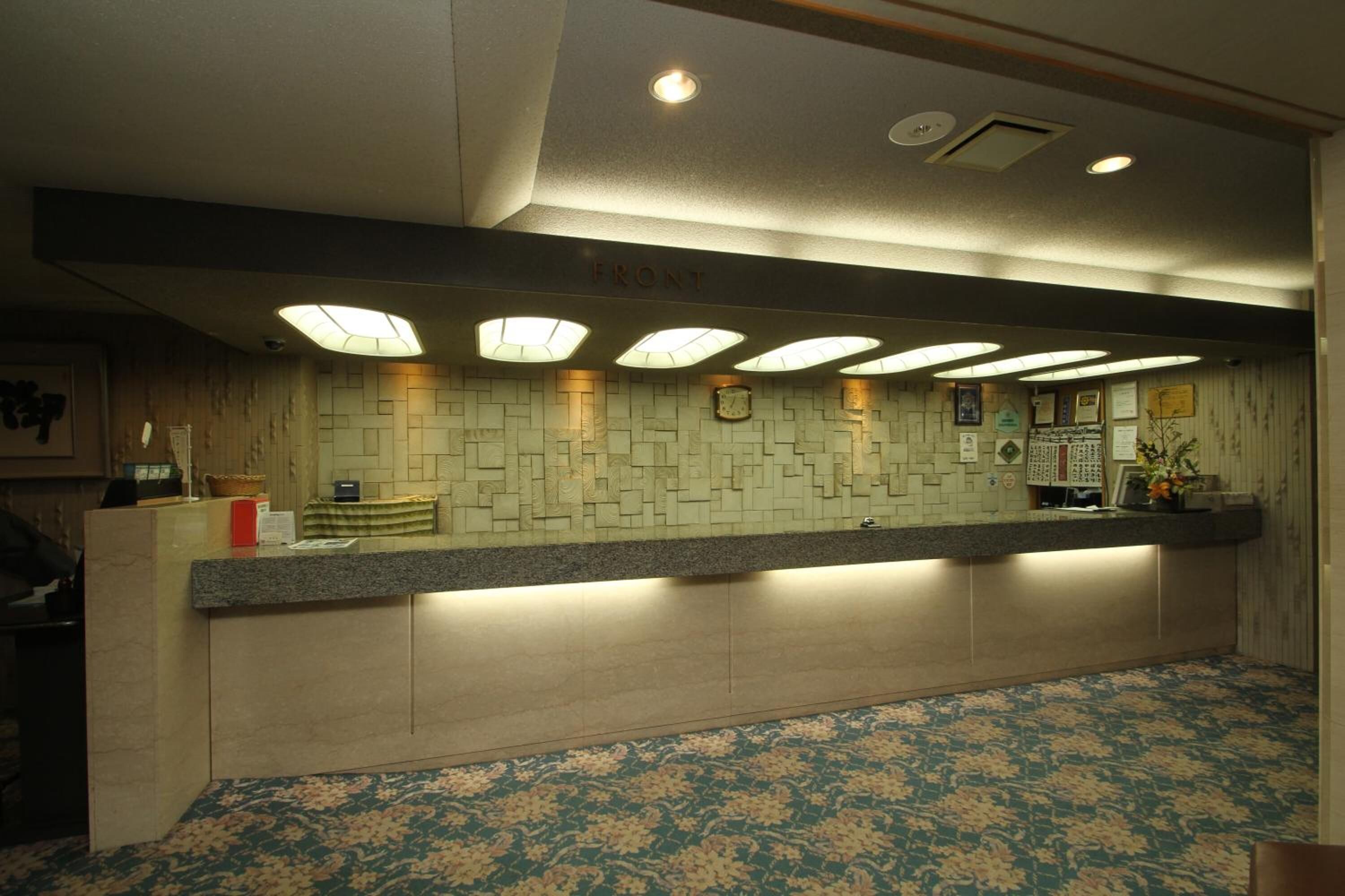 Un espace d’accueil d’hôtel avec un mur recouvert de carreaux, un comptoir d’accueil et une moquette à motifs.