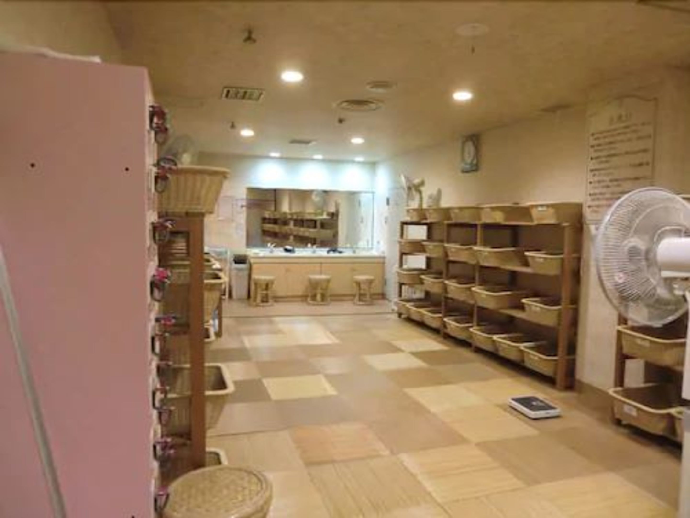 A room with a checkered floor, wooden shelves, a fan, and a counter with stools.