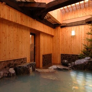 A wooden spa with a stone hot spring, wooden walls, and a tiled ceiling.