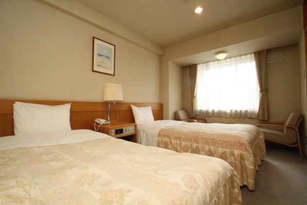A hotel room with two beds, a desk with a phone, a chair, and a window with curtains.