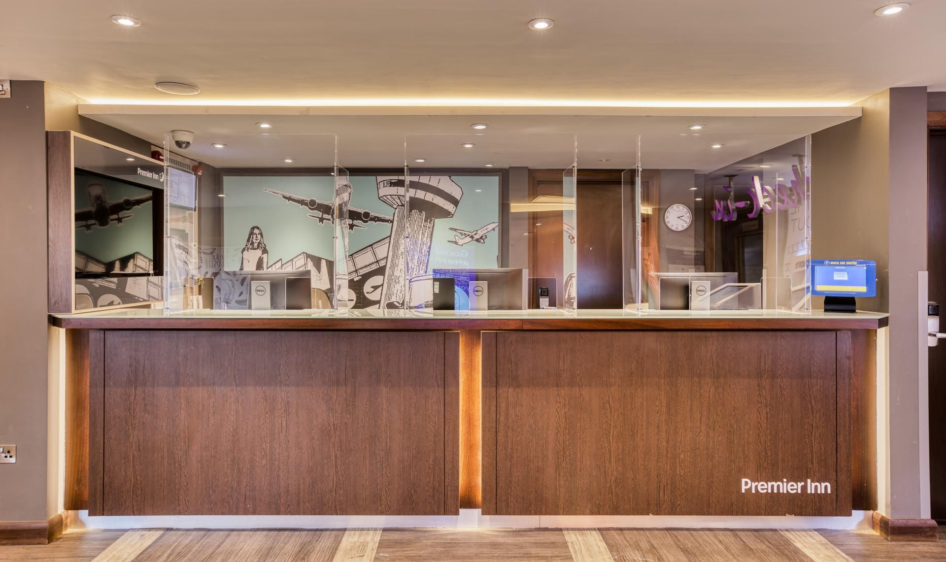 Een receptiebalie van een hotel met een digitaal scherm, een klok en een bord met de naam van het hotel.