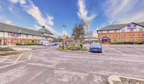 A Premier Inn hotel with a parking lot, a blue car in the foreground, and a clear sky. - Premier Inn London Beckton (London)