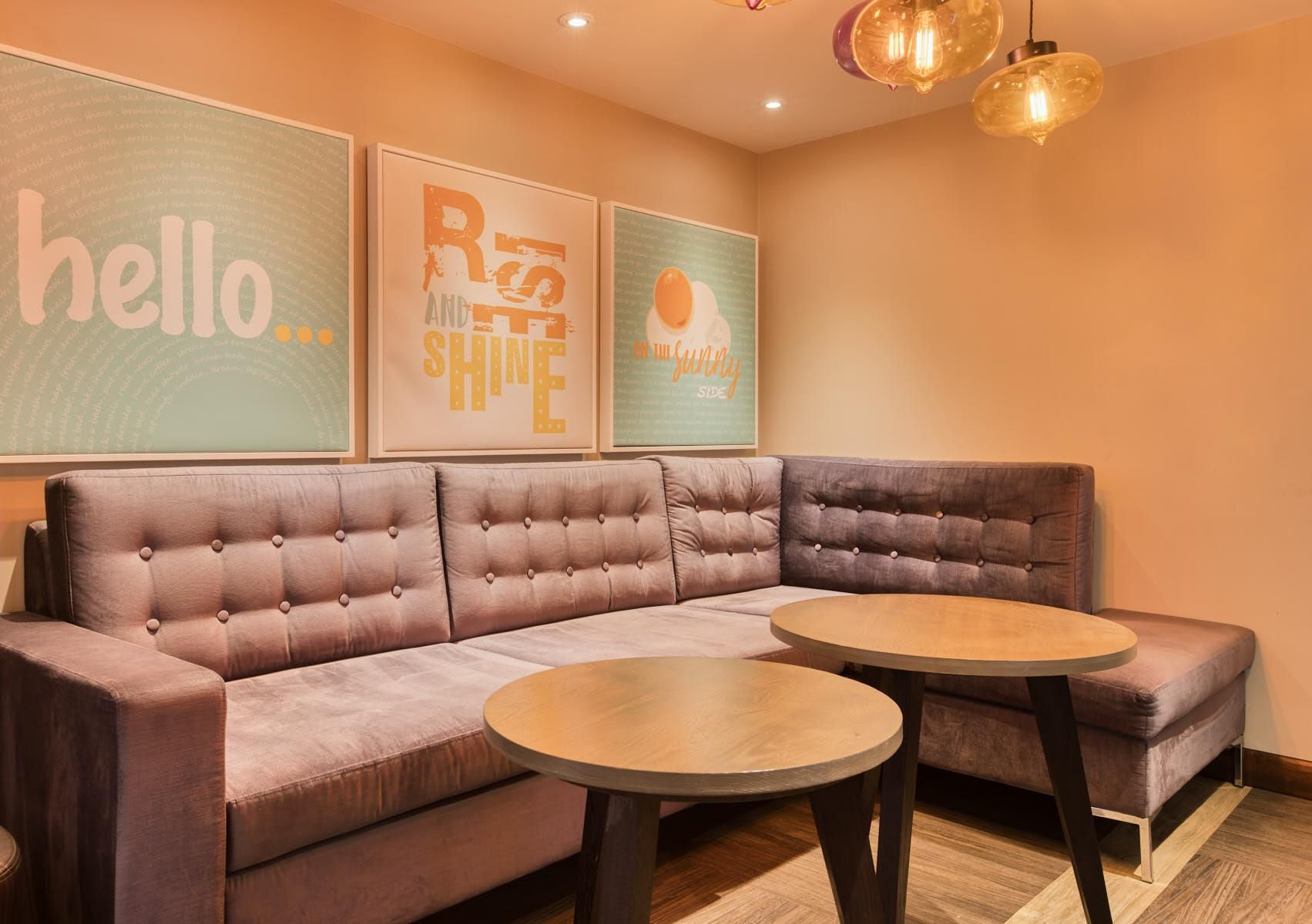 A modern lounge area with a sectional sofa, two round tables, and motivational wall art.