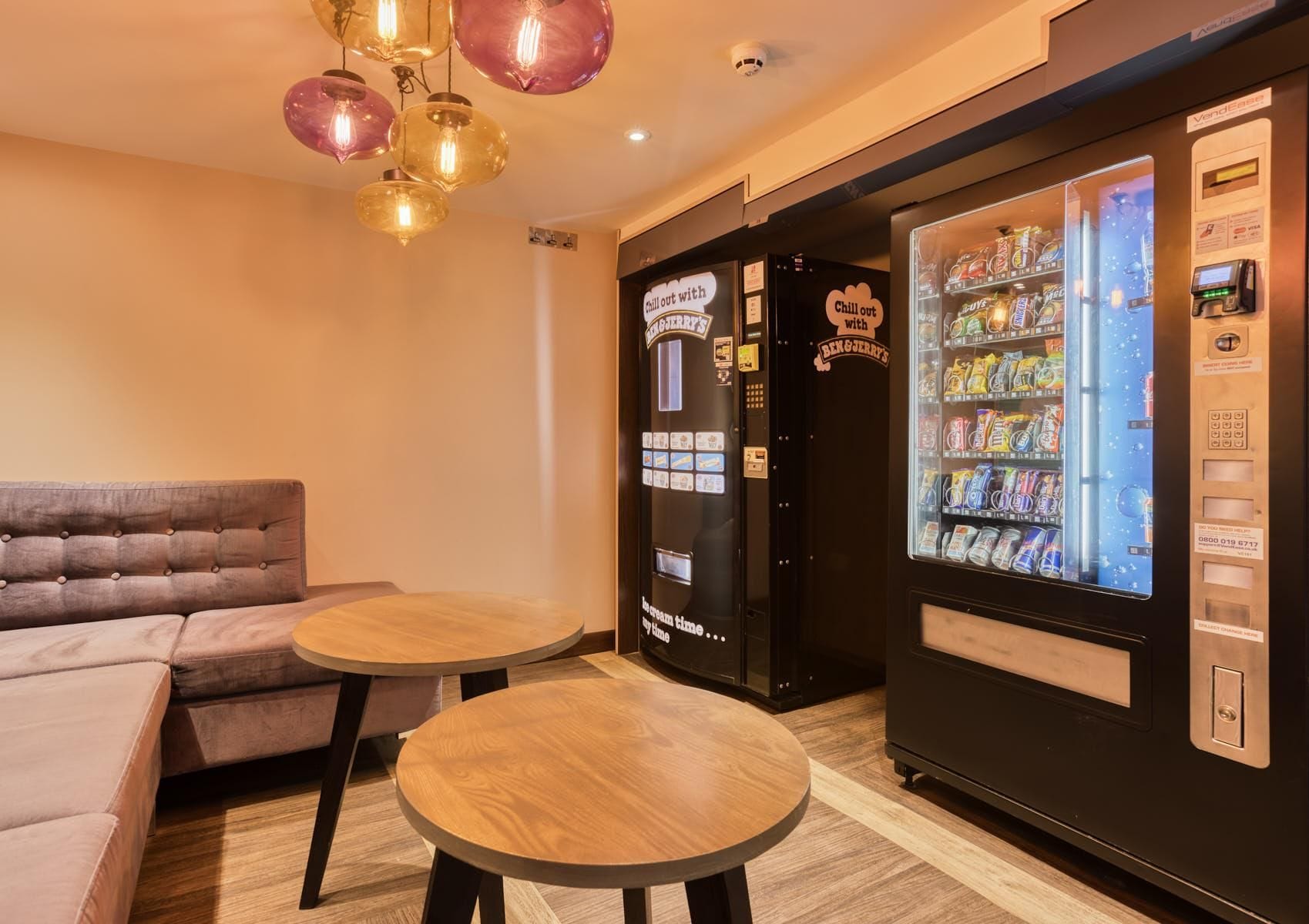A room with a sofa, two small wooden tables, and vending machines.