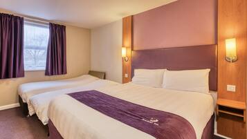 A hotel room with two beds, a headboard, bedside lamps, and a window with curtains.