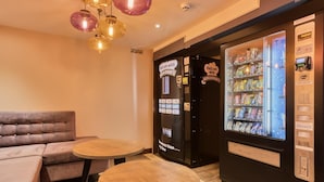 A room with a sofa, two small wooden tables, and vending machines. - Premier Inn London Beckton (London)