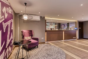 A hotel lobby with a reception desk, a purple armchair, a small table, and a patterned rug. - Premier Inn London Beckton (London)