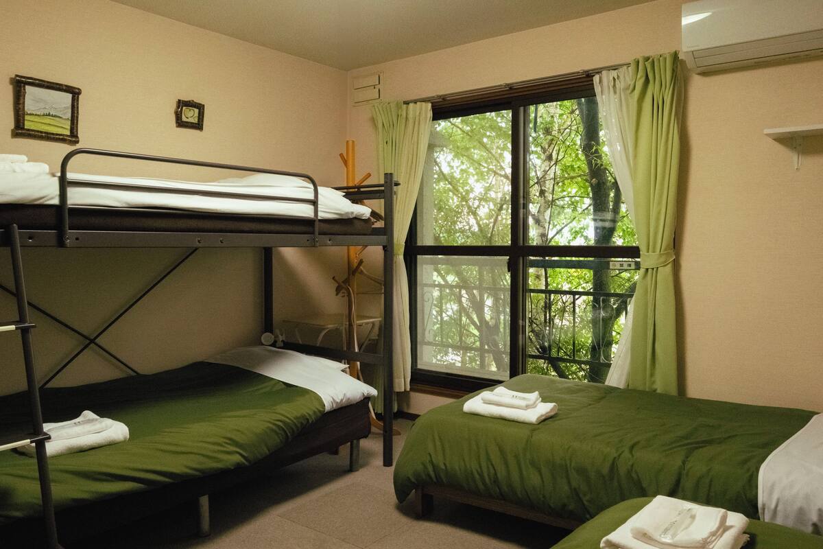 Une chambre de dortoir avec des lits superposés, une fenêtre avec des rideaux et un tableau encadré au mur.