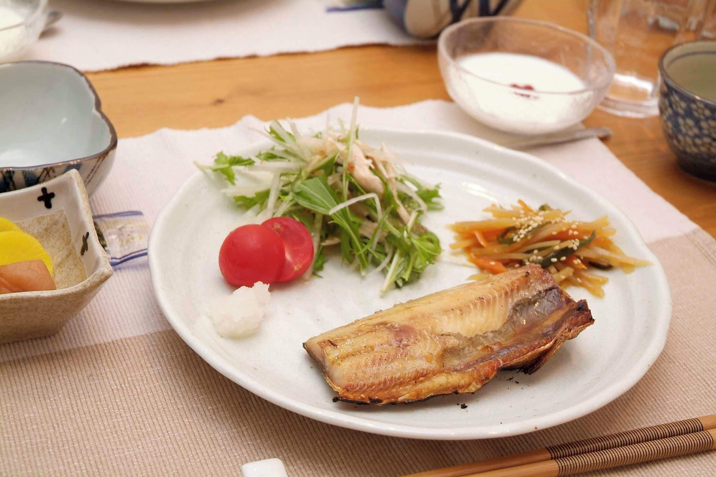 Un plato de comida con pescado, ensalada y un recipiente pequeño de salsa.