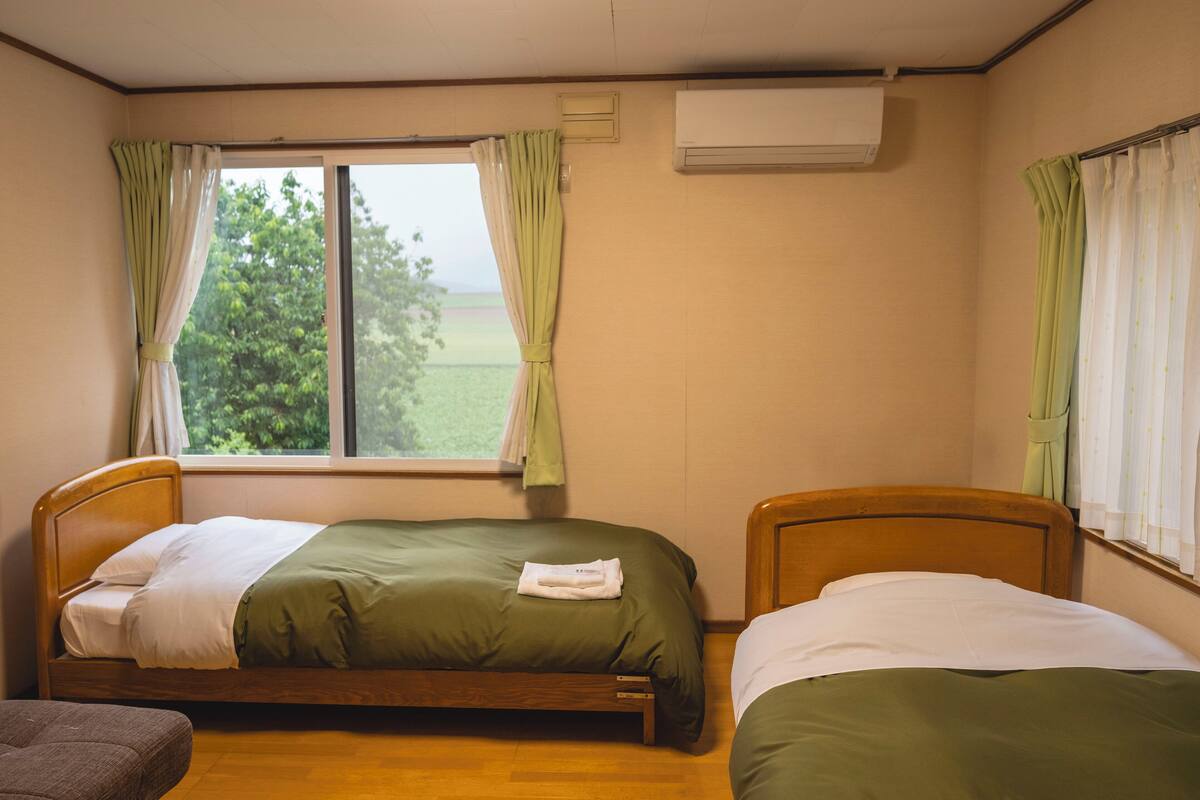 Une chambre avec deux lits simples, un plancher en bois, une fenêtre avec des rideaux et un appareil de climatisation.