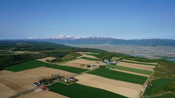 An aerial view of a rural landscape with fields, a small cluster of buildings, and snow-capped mountains in the background.