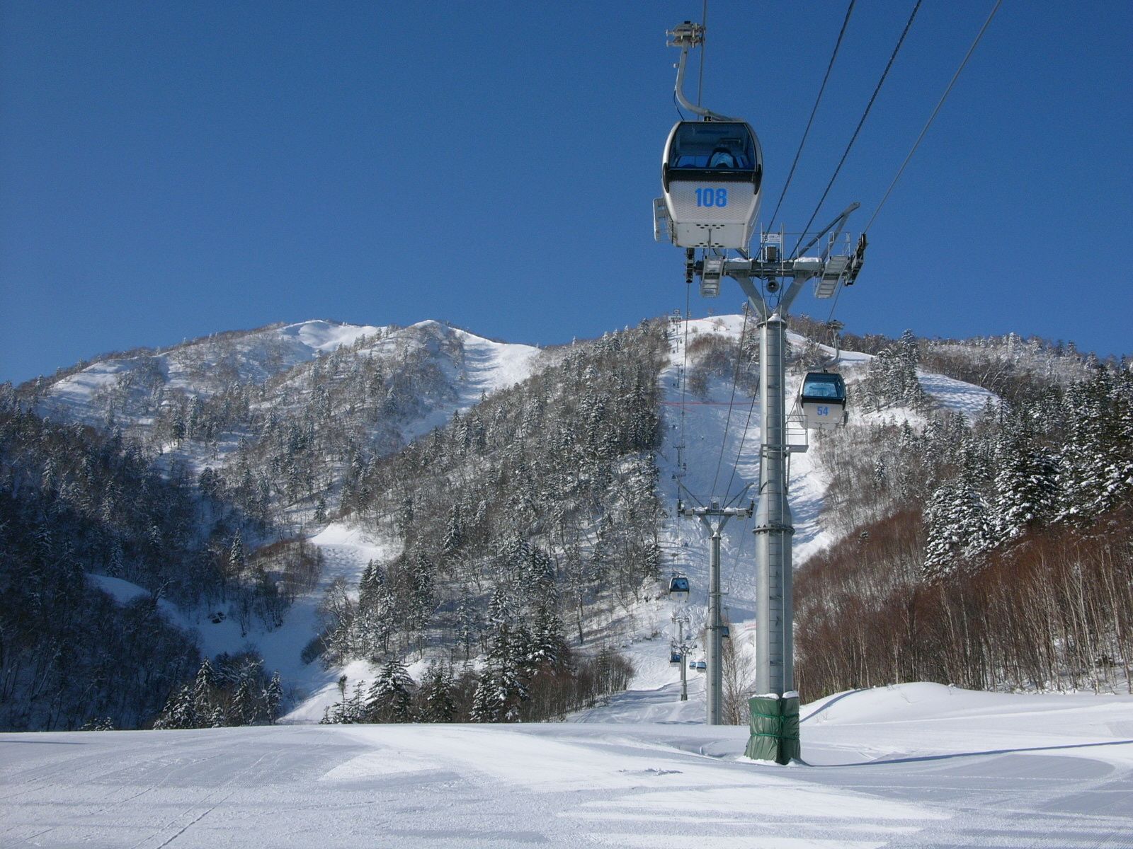 A ski lift with cabins numbered 108 and 54, a snowy mountain slope, and a clear sky.