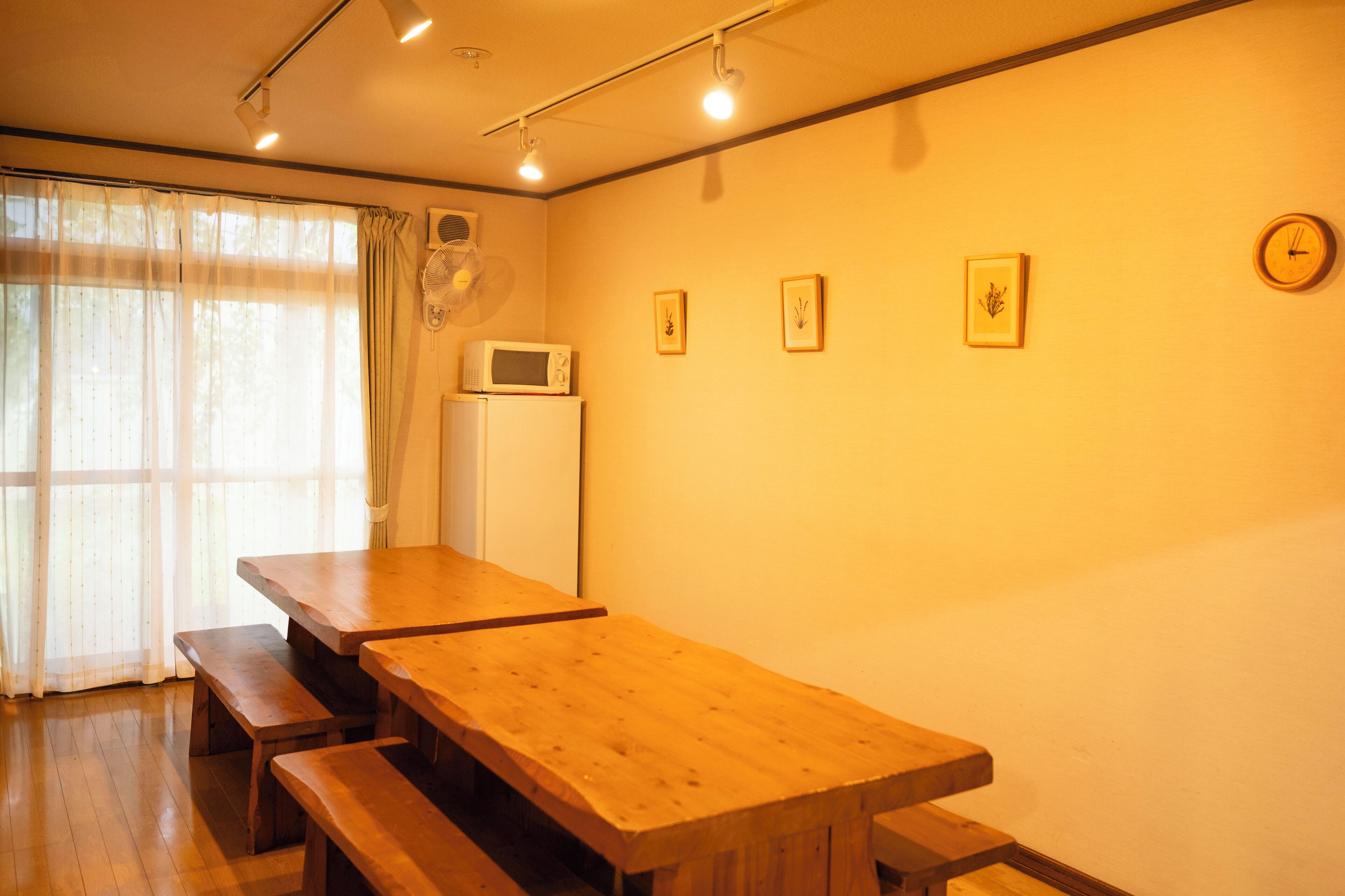 A room with a wooden table and benches, a microwave on a small white appliance, and a clock on the wall.