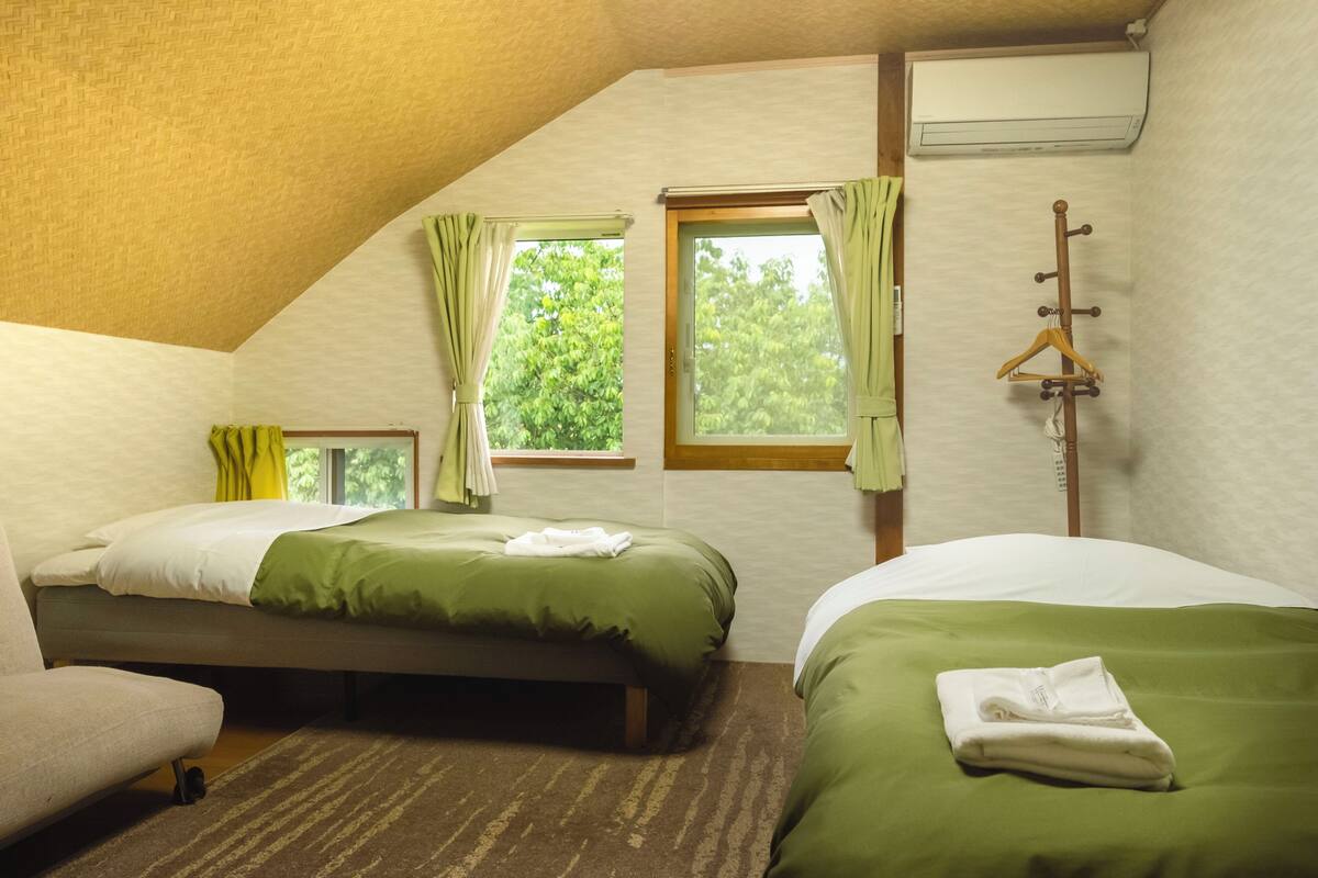 Une chambre avec deux lits, un canapé, un porte-manteau en bois et une fenêtre avec des rideaux.