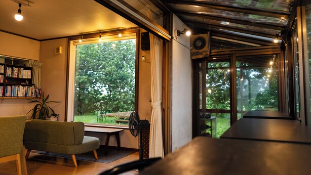 Un interior moderno con ventanas amplias, una estantería, un sillón verde y un ventilador de techo.