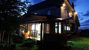 Una casa con porche cubierto, chimenea a la vista y un barril en el jardín.