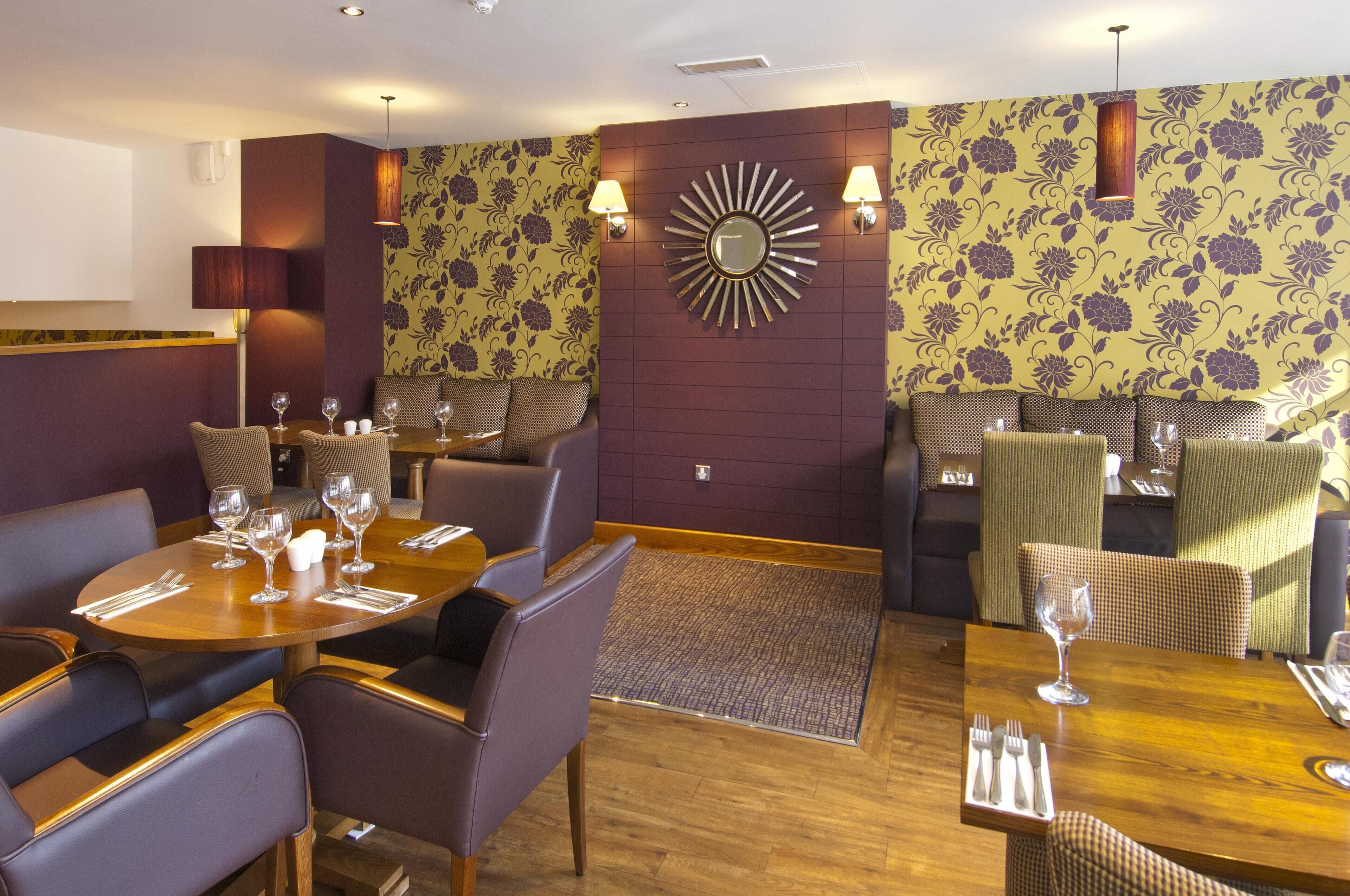 Een restaurant met ronde tafels, comfortabele stoelen en een behang met patroon.