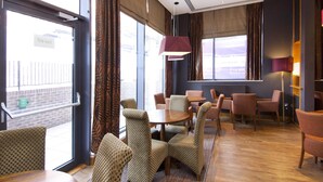 Une chambre d’hôtel avec un panneau indiquant la sortie de secours, des chaises à motifs, une table ronde et une grande fenêtre avec des rideaux.