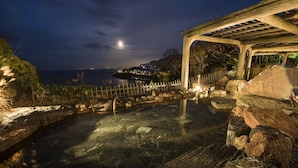 A clear pool with rocks and a wooden pergola at night.