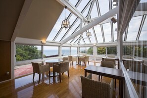 A spacious room with a high ceiling and large windows, featuring a round table and wicker chairs. - Ginrinsou (Otaru)