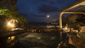 A nighttime view of a serene outdoor pool area with a wooden pergola and a clear view of the distant cityscape.