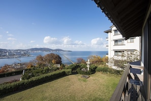 A residential area with a view of a body of water, a distant cityscape, and a white building with a balcony. - Ginrinsou (Otaru)