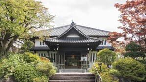 A traditional Japanese building with a tiled roof, a staircase leading to the entrance, and surrounding greenery. - Ginrinsou (Otaru)