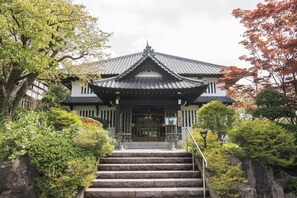 A traditional Japanese building with a tiled roof, a staircase leading to the entrance, and surrounding greenery. - Ginrinsou (Otaru)