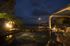 A nighttime view of a serene outdoor pool area with a wooden pergola and a clear view of the distant cityscape. - Ginrinsou (Otaru)