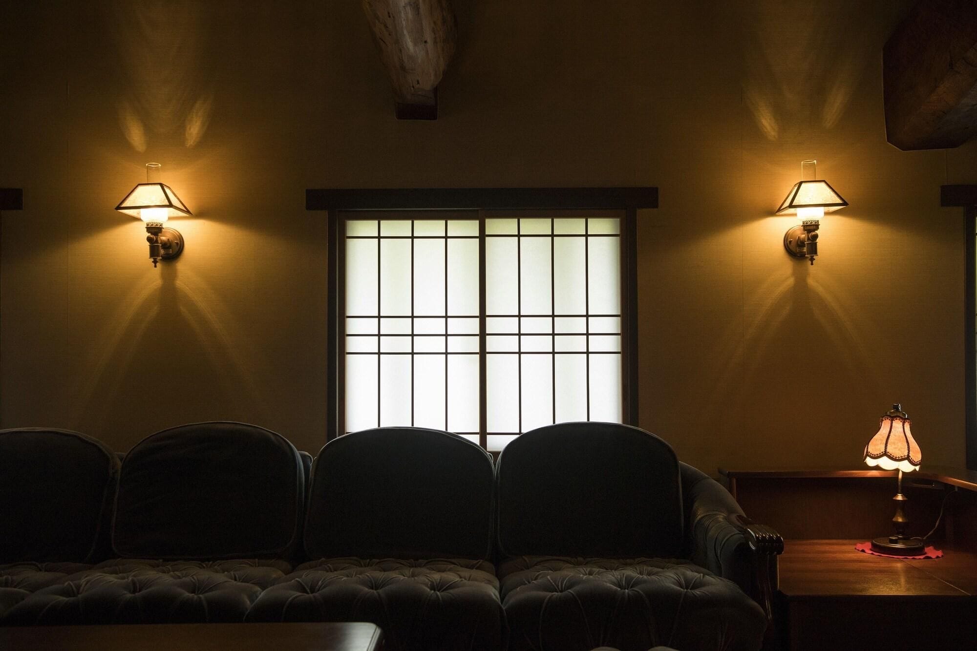 A dimly lit room with a sofa, two wall-mounted lamps, and a window with a grid pattern.
